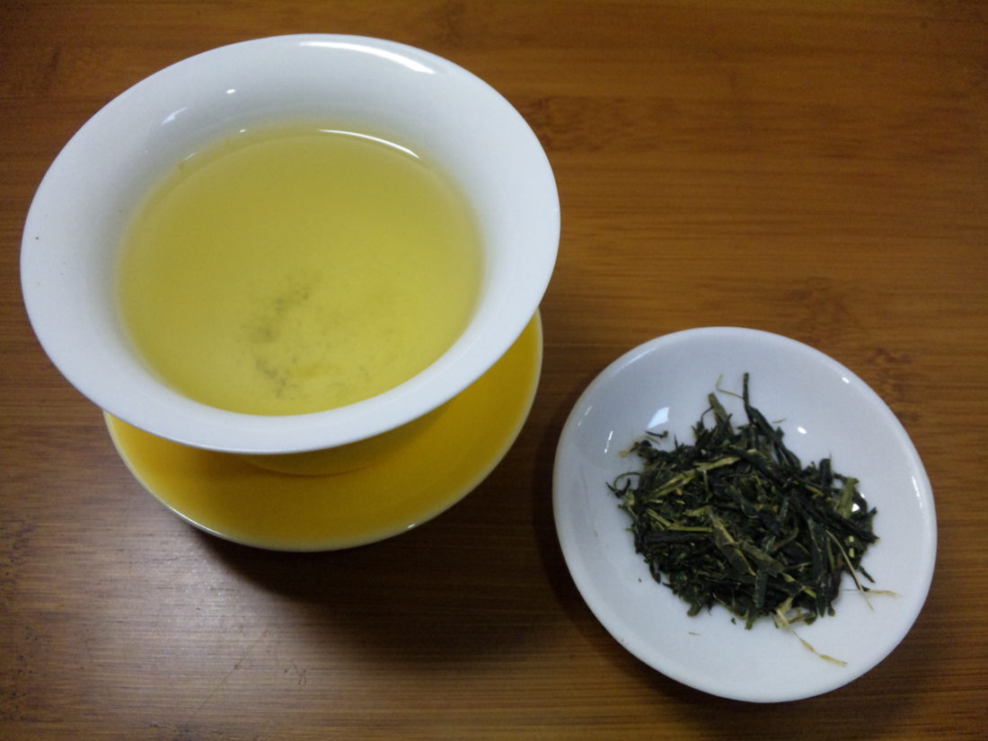 green tea leaves next to a cup of green tea